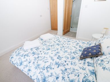 A bedroom with a bed with floral bedding two wooden doors and a small side table with a lamp at Kerangarth in Corbridge