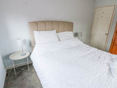 A bedroom with a double bed white bedding beige headboard two bedside tables with lamps and a closed door at Kerangarth in Corbridge