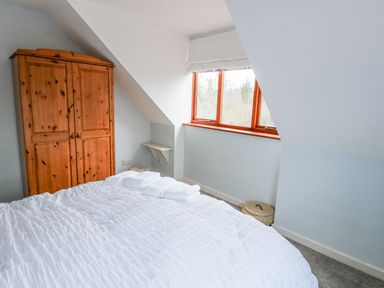 A bedroom with a white bedspread a wooden wardrobe a window and a small corner shelf at Kerangarth in Corbridge