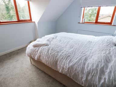 A bedroom with a bed covered in a white duvet and folded towels on top near two windows at Kerangarth in Corbridge