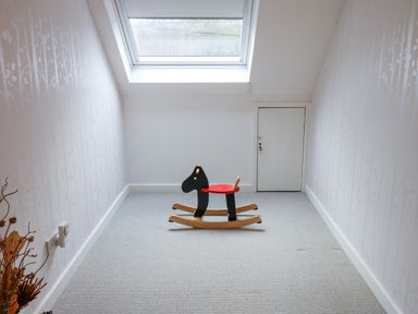 A small room with a skylight, a black and red rocking horse toy on a carpeted floor, and a closed door at the far end at Kerangarth in Corbridge