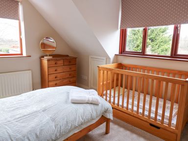 A bedroom with a wooden crib dresser with a round mirror and a bed with folded towels at Kerangarth in Corbridge