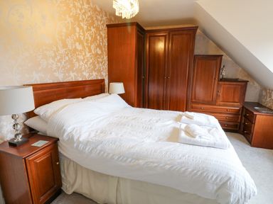 A bedroom with a double bed white bedding wooden bedside tables lamps and wooden wardrobes at Kerangarth in Corbridge