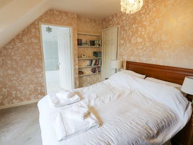 A bedroom with a double bed white bedding and towels on the bed a bookshelf and an open door leading to a bathroom at Kerangarth in Corbridge