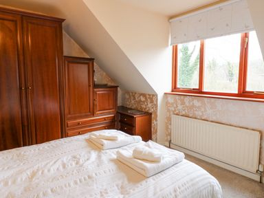 A bedroom with a bed with folded towels and wooden wardrobes near a window at Kerangarth in Corbridge