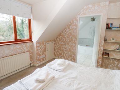 A bedroom with a bed and towels folded on it facing a window and an open door to a bathroom at Kerangarth in Corbridge
