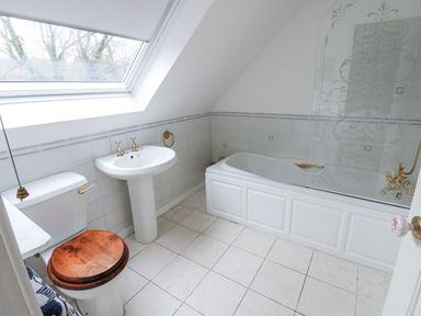 A bathroom with a toilet with wooden seat cover a pedestal sink a bathtub with a glass shower screen and a skylight window at Kerangarth in Corbridge