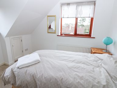 A bedroom with a bed covered with blankets a folded towel on the bed a window with patterned blind a small wooden nightstand with a blue lamp and a wall mirror at Kerangarth in Corbridge