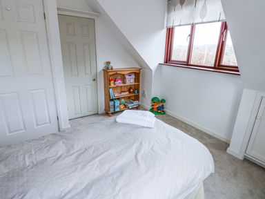 A bedroom with a bed a wooden bookshelf with toys and a window with curtains at Kerangarth in Corbridge