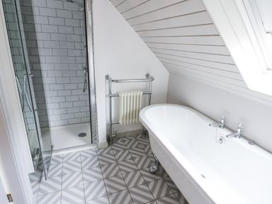A bathroom with a bathtub a glass shower enclosure a towel radiator and patterned tile floor at Kerangarth in Corbridge