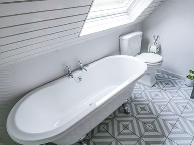 A bathroom with a bathtub under a skylight and a toilet on patterned tiled floor at Kerangarth in Corbridge