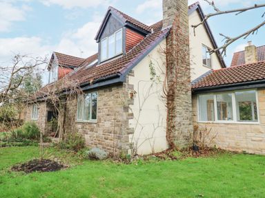 A stone and brick house with a tiled roof and windows surrounded by a green lawn and leafless trees at Kerangarth in Corbridge