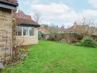 A garden with green grass and shrubs next to a stone house with tiled roof at Kerangarth in Corbridge