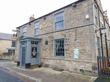 Stone building with a gray door and windows and a sign reading The Dyvels at Kerangarth in Corbridge