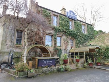 An exterior view of a building covered with ivy with a wooden sheltered seating area and planters outside at The Valley in Corbridge