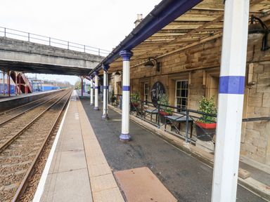 A train platform with tracks next to a covered area with columns and potted plants at Kerangarth in Corbridge