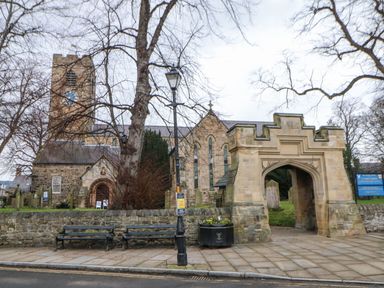 A stone church with a clock tower and arched entrance surrounded by a stone wall with benches and a lamppost outside at Kerangarth in Corbridge