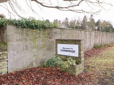 A stone wall with a welcome to Corbridge sign and plants at Kerangarth in Corbridge