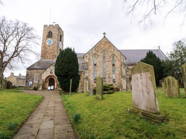A stone church with a clock tower surrounded by gravestones and a paved pathway at Kerangarth in Corbridge