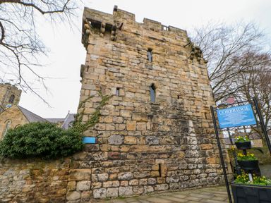 A stone tower structure with narrow windows next to a sign and flowers in Corbridge