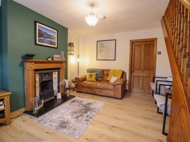 A living room with a fireplace a brown leather sofa and a wooden staircase at Gwynfa in Ysbyty Ifan