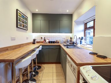 A kitchen with wooden countertops and gray cabinets with stools by a breakfast bar at Gwynfa in Ysbyty Ifan