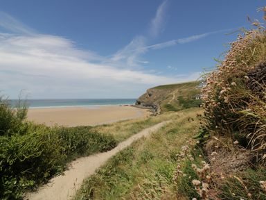A sandy beach with a coastal path and cliffs under a blue sky at The Cow Shed in Porthcothan near Mawgan Porth
