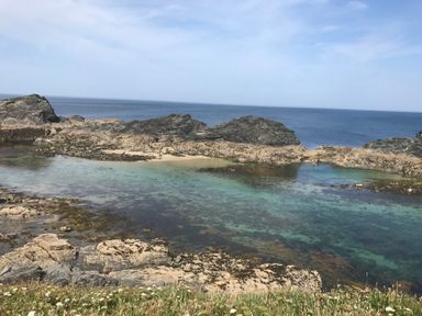 A coastal scene with rocky shore and clear water at The Cow Shed in Porthcothan near Mawgan Porth