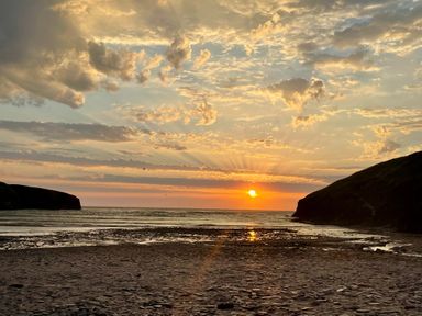 A sunset over the ocean with clouds and birds above a rocky shore at The Cow Shed in Porthcothan near Mawgan Porth