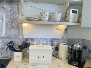 A kitchen with shelving, bowls, utensils, a kettle and a coffee machine at The Cow Shed in Mawgan Porth