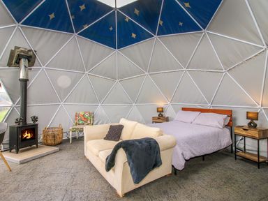 A dome-shaped room with a bed, sofa, wood burning stove, and a small chair at Meadow View - Bryn-Mawr Retreat in Brynmawr near Llanymynech