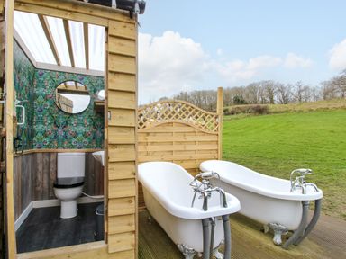 An outdoor bathroom with two white clawfoot bathtubs and a wooden structure housing a toilet and sink at Meadow View - Bryn-Mawr Retreat in Brynmawr near Llanymynech