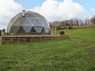 A geodesic dome on a wooden raised platform in a grassy field with trees in the background at Meadow View - Bryn-Mawr Retreat in Brynmawr near Llanymynech