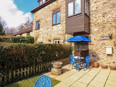 An outdoor patio with a blue table and chairs under a blue umbrella next to a stone house at Millers Loft in Modbury