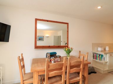 A dining area with a wooden table and chairs a large mirror on the wall books and appliances on a kitchen counter at Millers Loft in Modbury