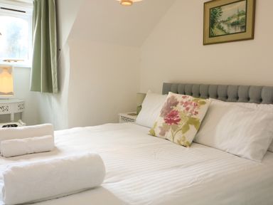 A bedroom with a bed with white linens and floral pillow near a window with green curtains at Millers Loft in Modbury
