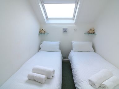 A small bedroom with two single beds under a skylight each bed has white linens rolled towels and a stuffed animal on a shelf at Millers Loft in Modbury