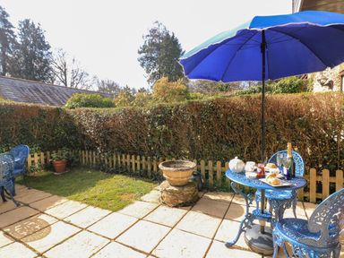 An outdoor patio with blue metal table and chairs under a blue umbrella with tea and scones on the table at Millers Loft in Modbury