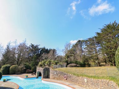 An outdoor swimming pool next to a stone wall and trees at Millers Loft in Modbury