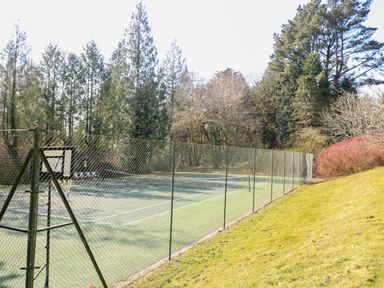 An outdoor tennis court surrounded by a chain link fence with trees and bushes around at Millers Loft in Modbury