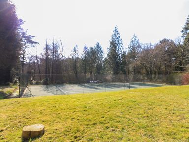 A fenced tennis court surrounded by trees and grass at Millers Loft Modbury