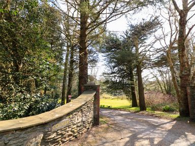 A stone wall with a sign that says Colmer and a driveway leading into a wooded area at Millers Loft in Modbury