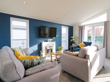 A living room with sofas a TV on a blue wall and sliding doors at Number 43 The Poplars in Burnham Market
