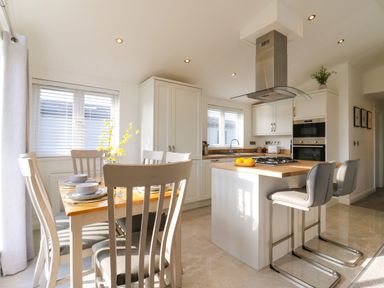 A kitchen and dining area with a wooden dining table, chairs, kitchen island with bar stools, stove, and cabinets at Number 43 The Poplars in Burnham Market