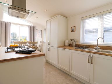 A kitchen with white cabinets a gas stove and a dining area with chairs at Number 43 The Poplars in Burnham Market