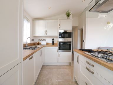 A kitchen with white cabinets wooden countertops a built in oven a gas stove and a sink at Number 43 The Poplars in Burnham Market