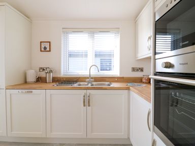 A kitchen with white cabinets a wooden countertop a sink a dish rack a kettle and built in ovens at Number 43 The Poplars in Burnham Market