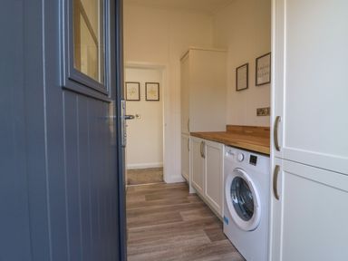 A laundry room with a washing machine wooden countertop white cabinets and wall art at Number 43 The Poplars Burnham Market