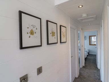 A hallway with three framed pictures on the wall and a carpeted floor at Number 43 The Poplars in Burnham Market