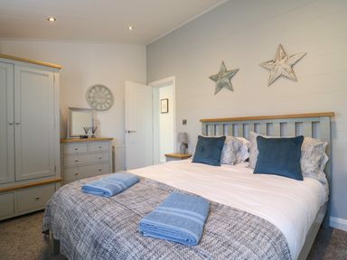 A bedroom with a bed set with pillows and towels a wardrobe a dresser with a mirror and a wall clock at Number 43 The Poplars in Burnham Market